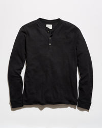 A black long-sleeve henley shirt with a three-button placket, laid flat against a light gray background.
