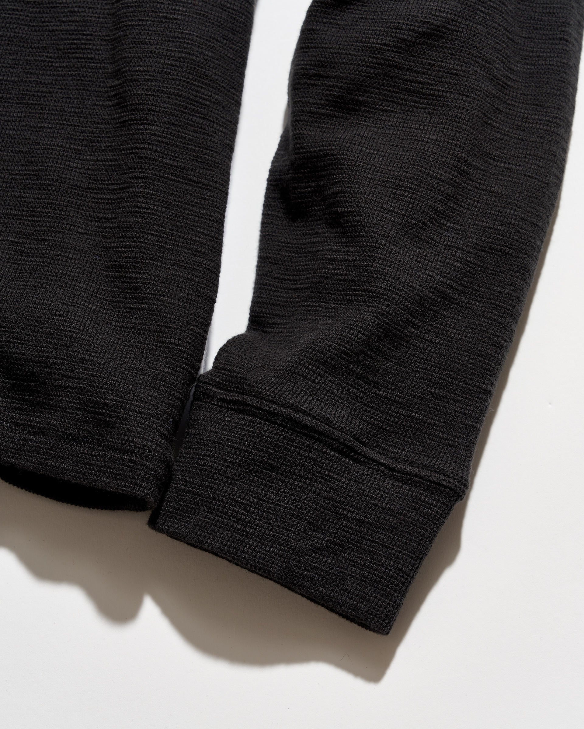 Close-up of a black ribbed knit garment sleeve with a folded cuff, shown on a white background with a soft shadow.