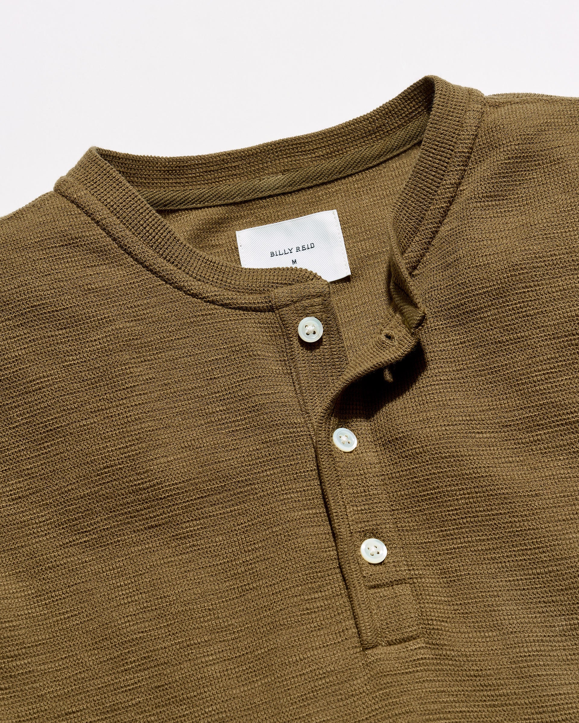 Close-up of a ribbed Henley shirt in olive brown with a white button placket and a visible 'BERRY RARE' neck label.