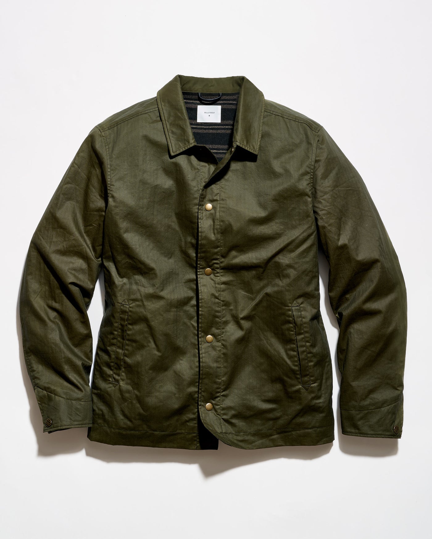 An olive green waxed cotton jacket with a button-up front, laid flat against a white background.