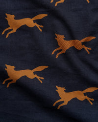 Close-up of a navy blue fabric with a repeating pattern of running foxes in a warm tan or camel color.