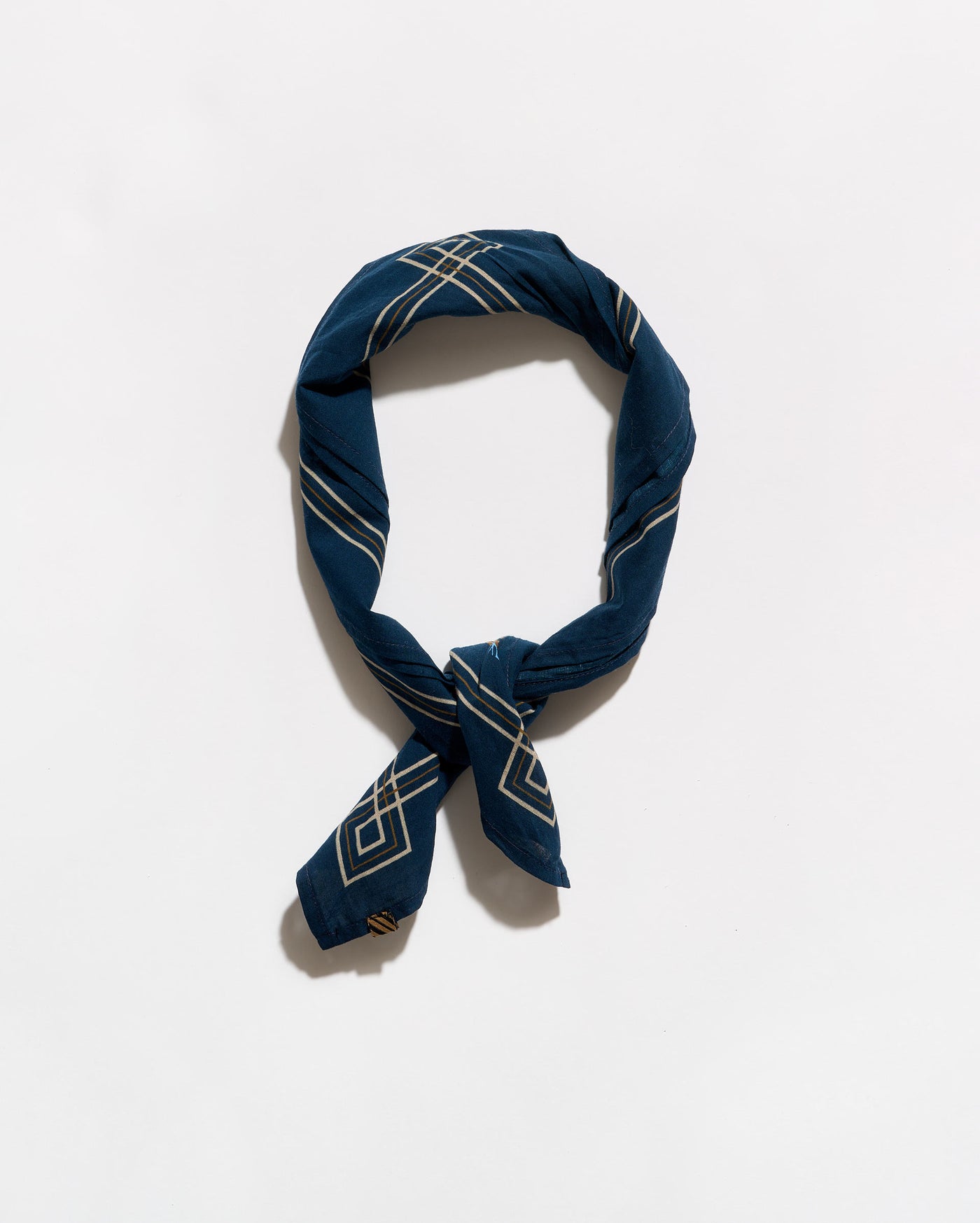 A navy blue silk scarf with a white geometric pattern, tied in a loop and knot, displayed on a clean white background.
