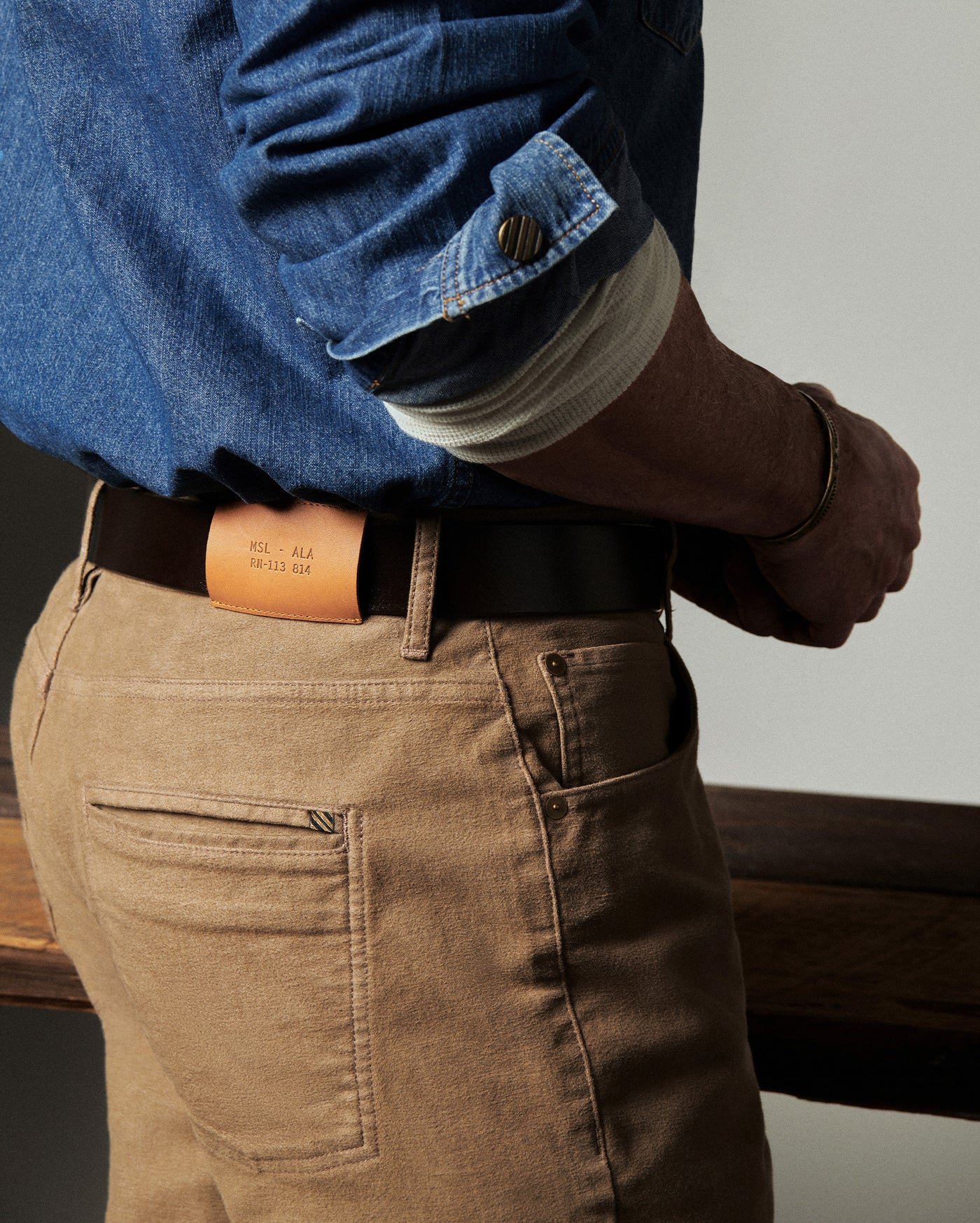 Person wearing a blue shirt, brown pants, and a leather belt with a visible brand name.
