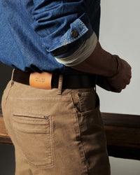 Person wearing a blue shirt, brown pants, and a leather belt with a visible brand name.