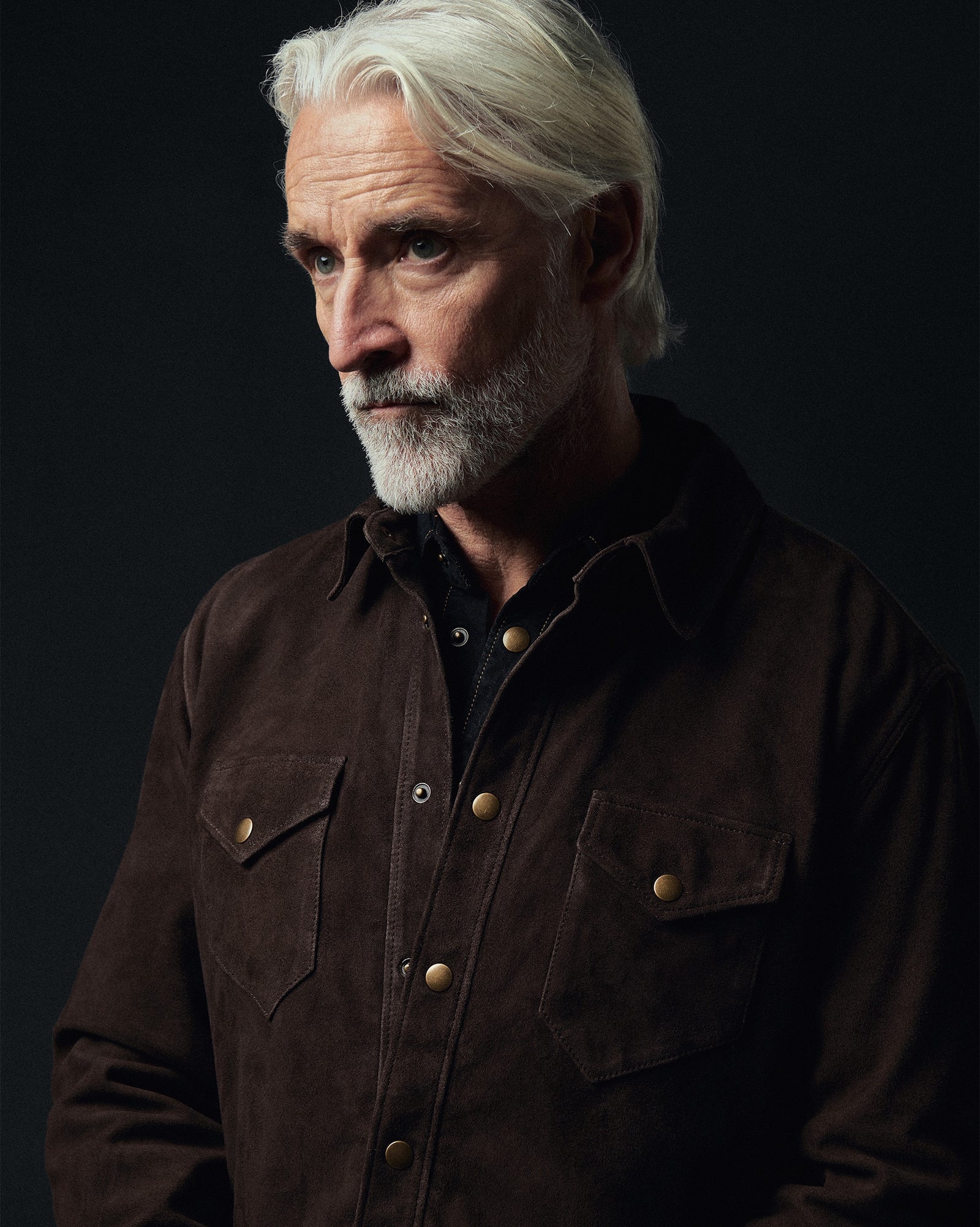 Man wearing a brown jacket with gold buttons against a dark background