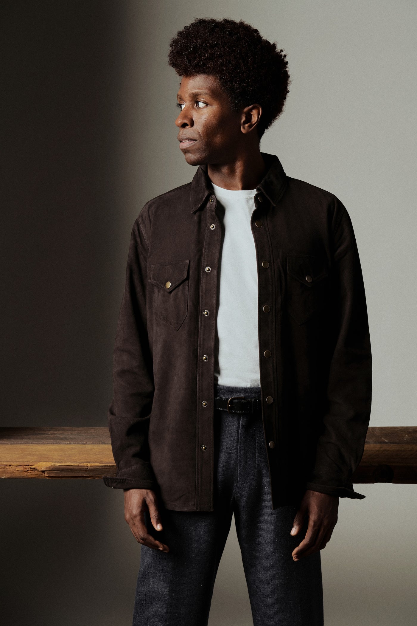Man wearing a dark brown jacket over a white shirt with a plain background