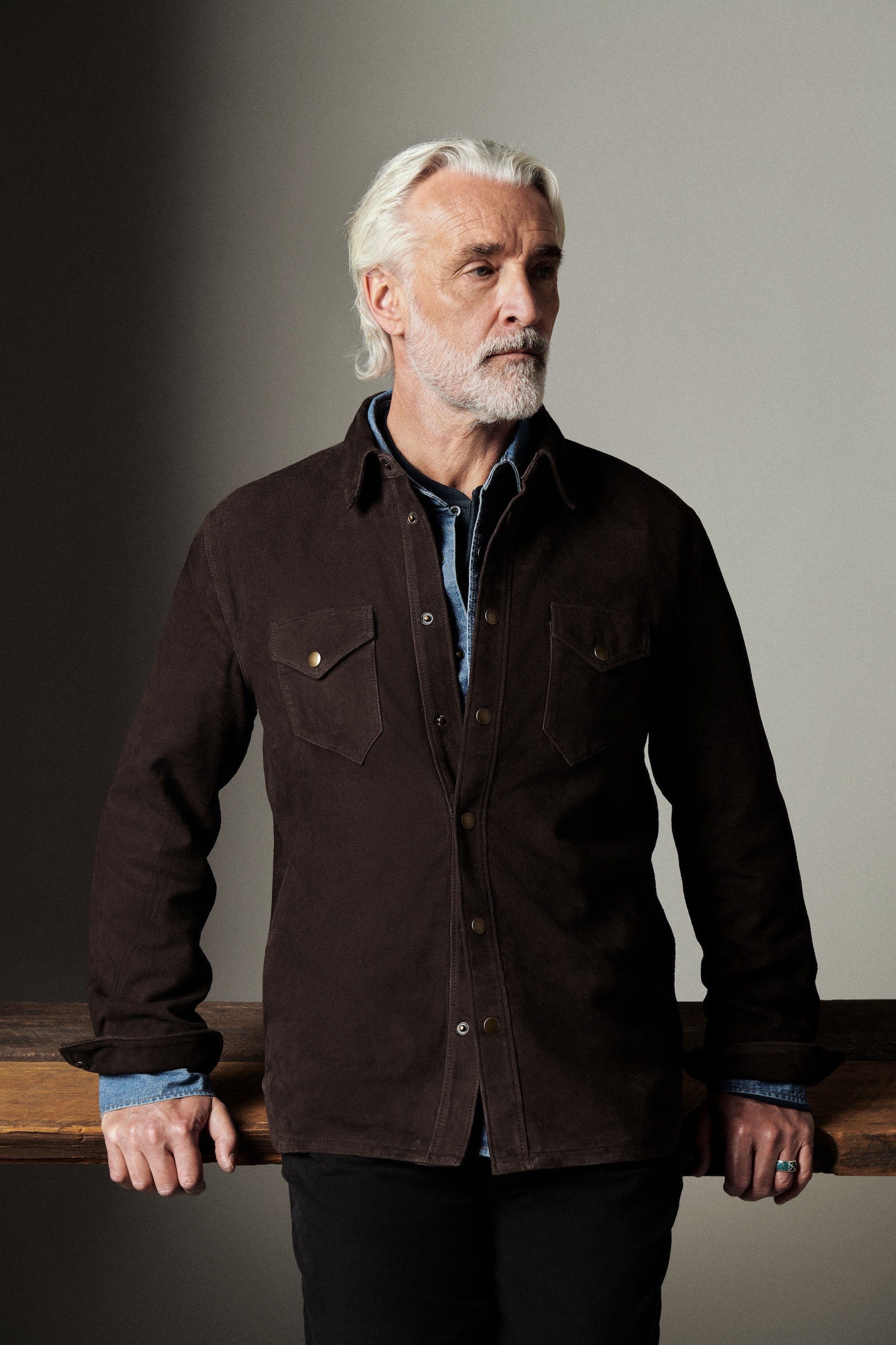 Man wearing a dark brown jacket against a neutral background