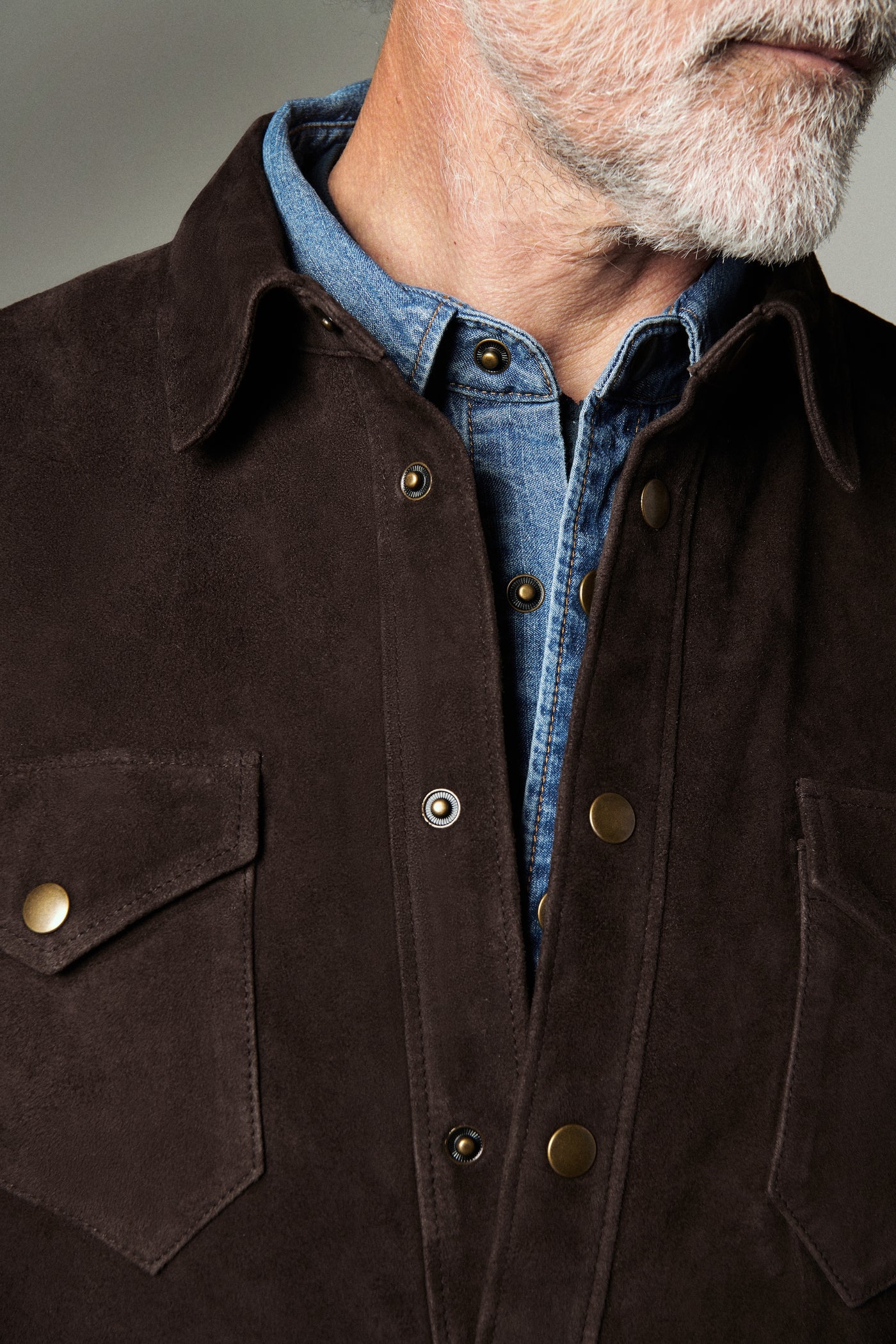 Close-up of a person wearing a dark brown jacket with a blue shirt underneath.