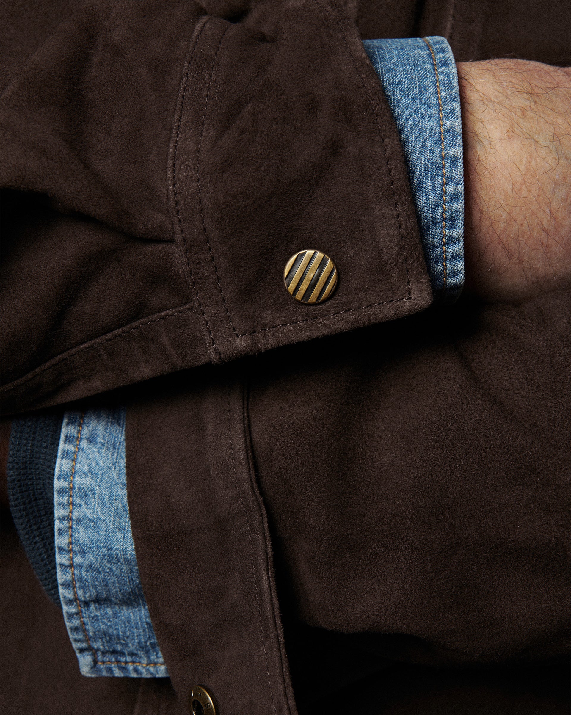 Close-up of a brown jacket with blue denim trim and gold button.