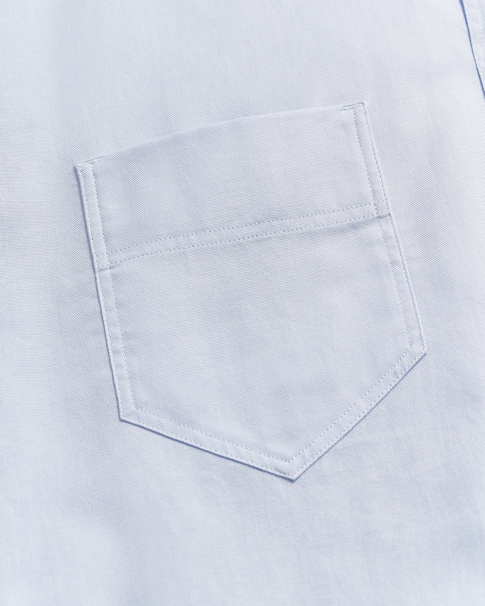 Close-up of a light blue fabric with a single, neatly stitched chest pocket visible in the center of the image.