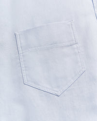 Close-up of a light blue fabric with a single, neatly stitched chest pocket visible in the center of the image.
