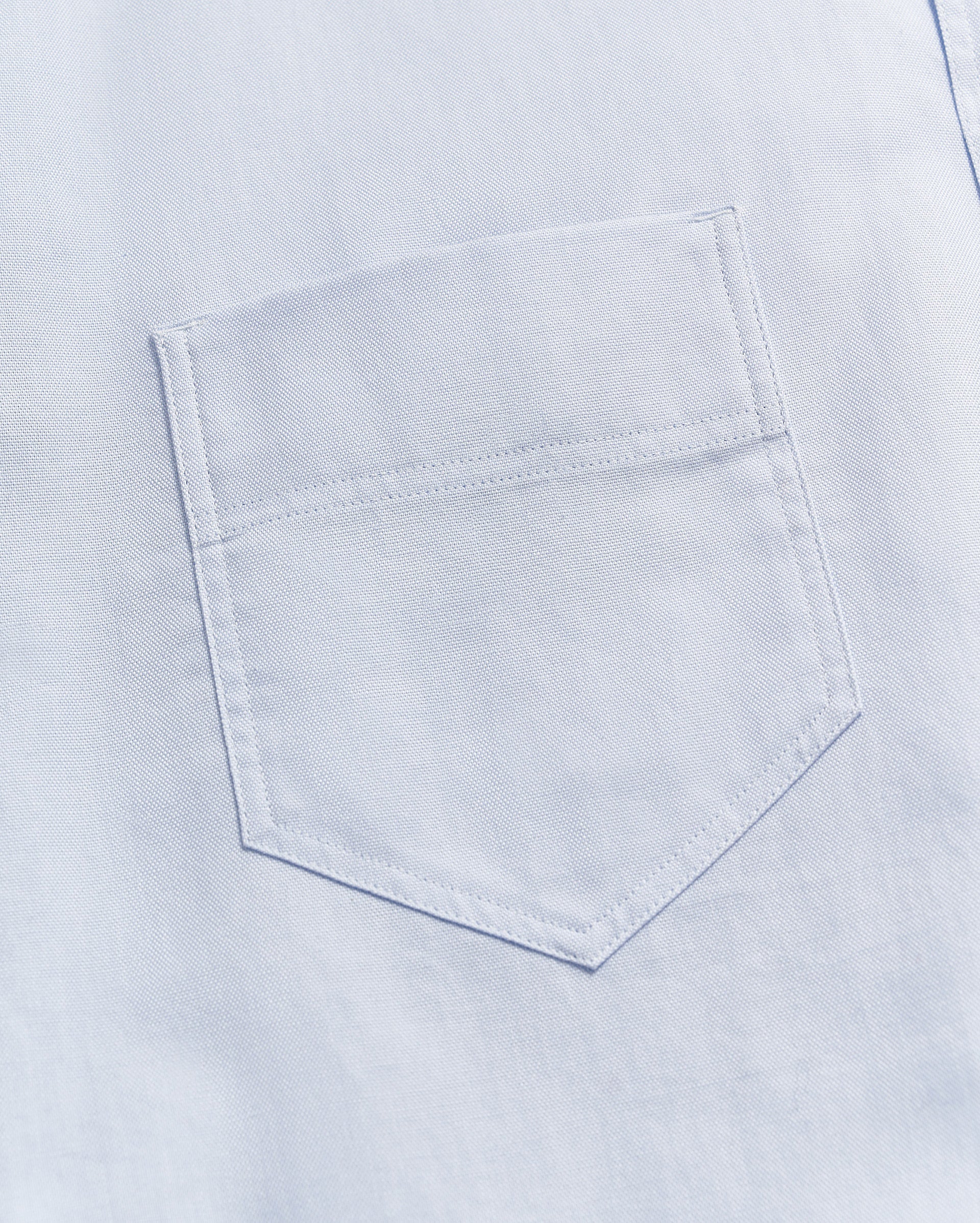 Close-up of a light blue fabric with a single, neatly stitched chest pocket visible in the center of the image.