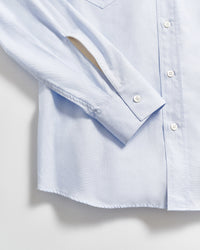 A close-up of a light blue button-up shirt, showing the sleeve, cuff with a button, and part of the front with white buttons against a plain background.