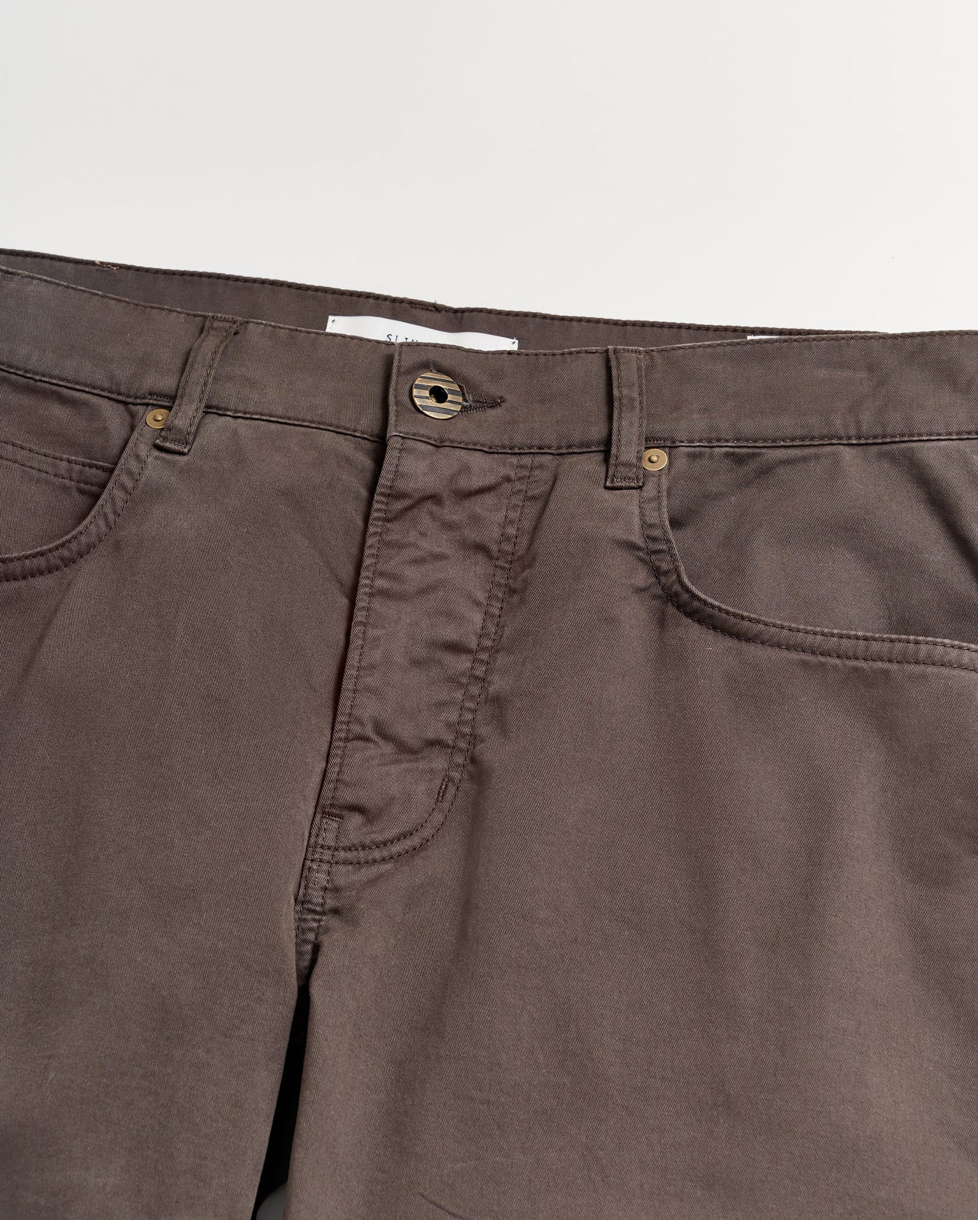 A close-up view of the waistband and upper section of brown pants with visible pockets, belt loops, and a button closure against a white background.