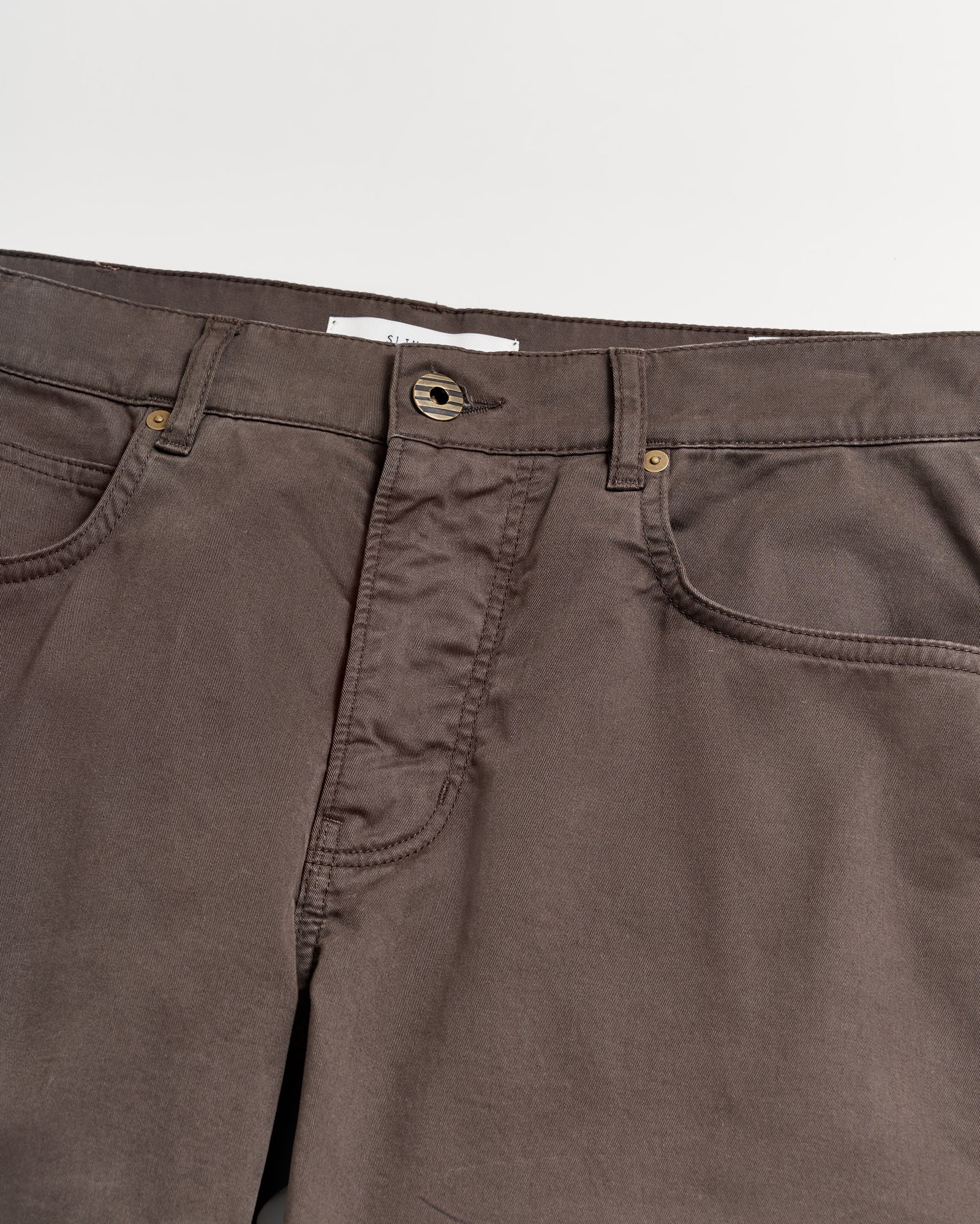 A close-up view of the waistband and upper section of brown pants with visible pockets, belt loops, and a button closure against a white background.