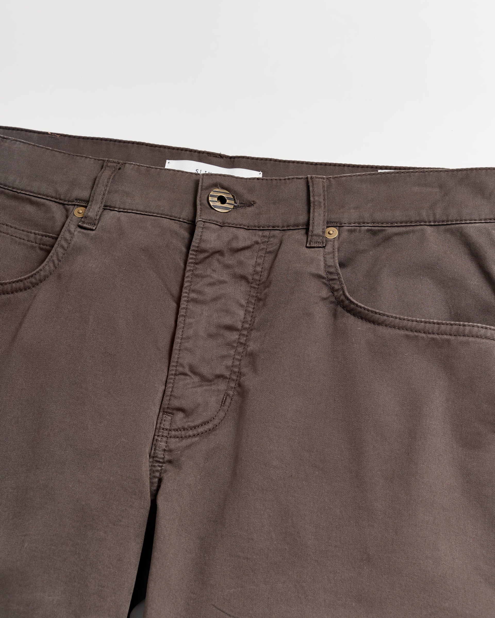 A close-up view of the waistband and upper section of brown pants with visible pockets, belt loops, and a button closure against a white background.