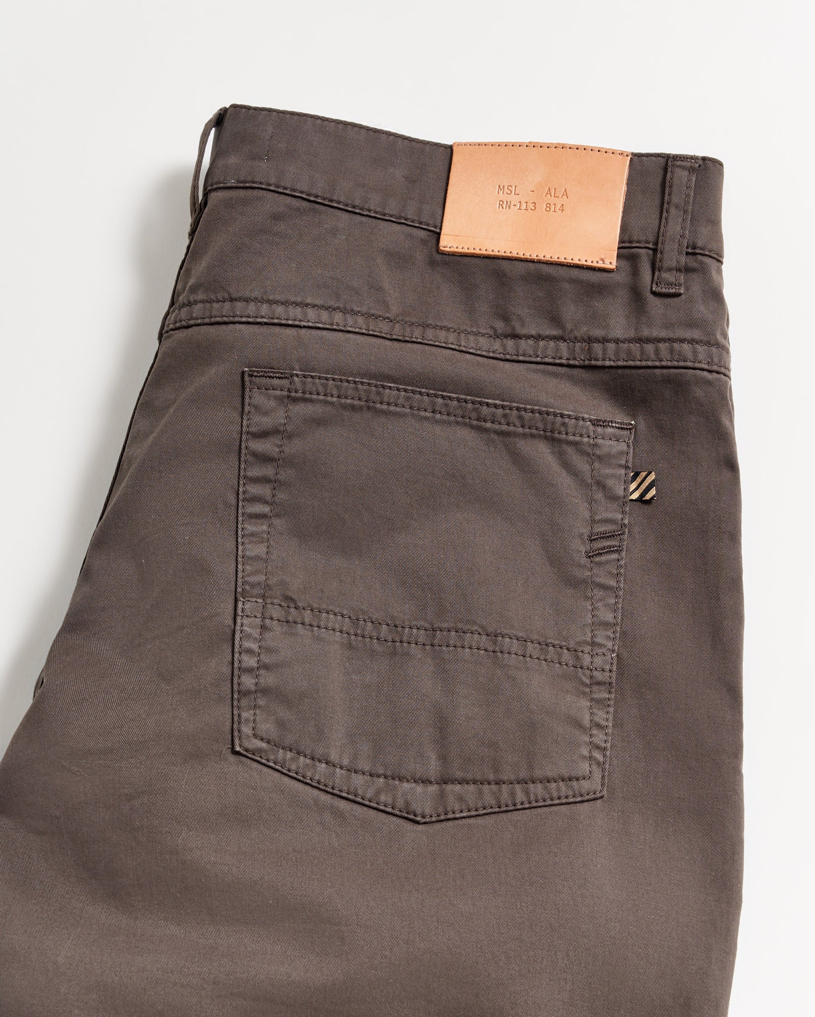 A close-up of the back of a pair of dark brown pants with a single back pocket and a tan leather patch on the waistband, shown on a white background.