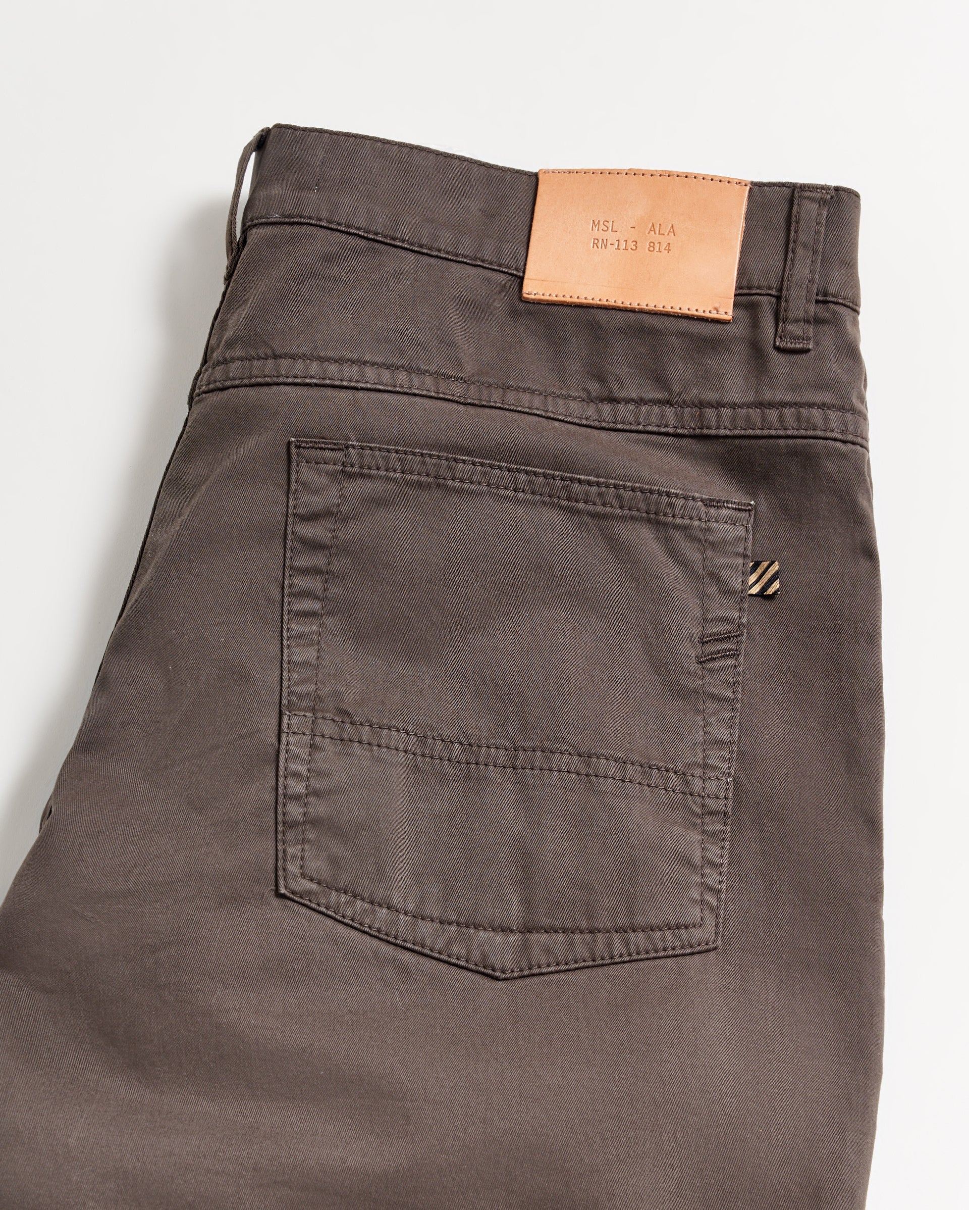 A close-up of the back of a pair of dark brown pants with a single back pocket and a tan leather patch on the waistband, shown on a white background.