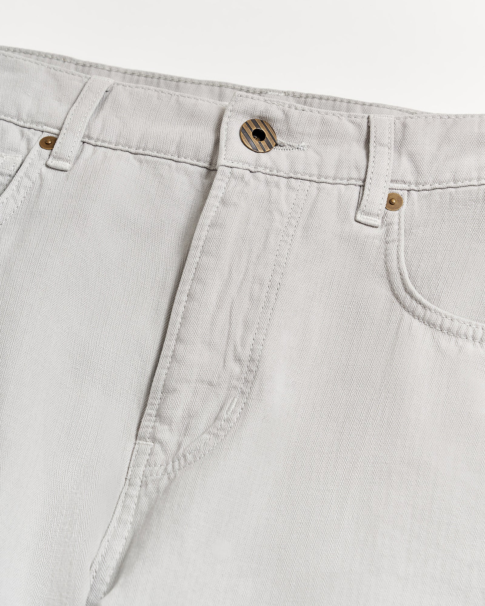 Close-up of the waist and upper leg area of light grey jeans with visible stitching, belt loops, a front button, and part of the pockets on a white background.