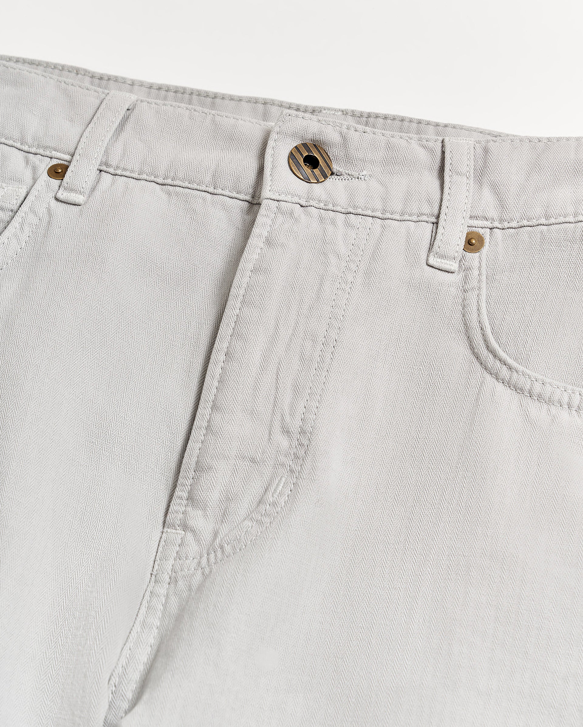 Close-up of the waist and upper leg area of light grey jeans with visible stitching, belt loops, a front button, and part of the pockets on a white background.