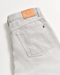 A close-up of the back pocket and waistband of light gray jeans with a tan leather patch featuring embossed lettering, laid flat on a white surface.