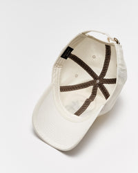 An upside-down white baseball cap with visible brown stitching on the inside, a black label, and an adjustable strap, displayed on a white background.