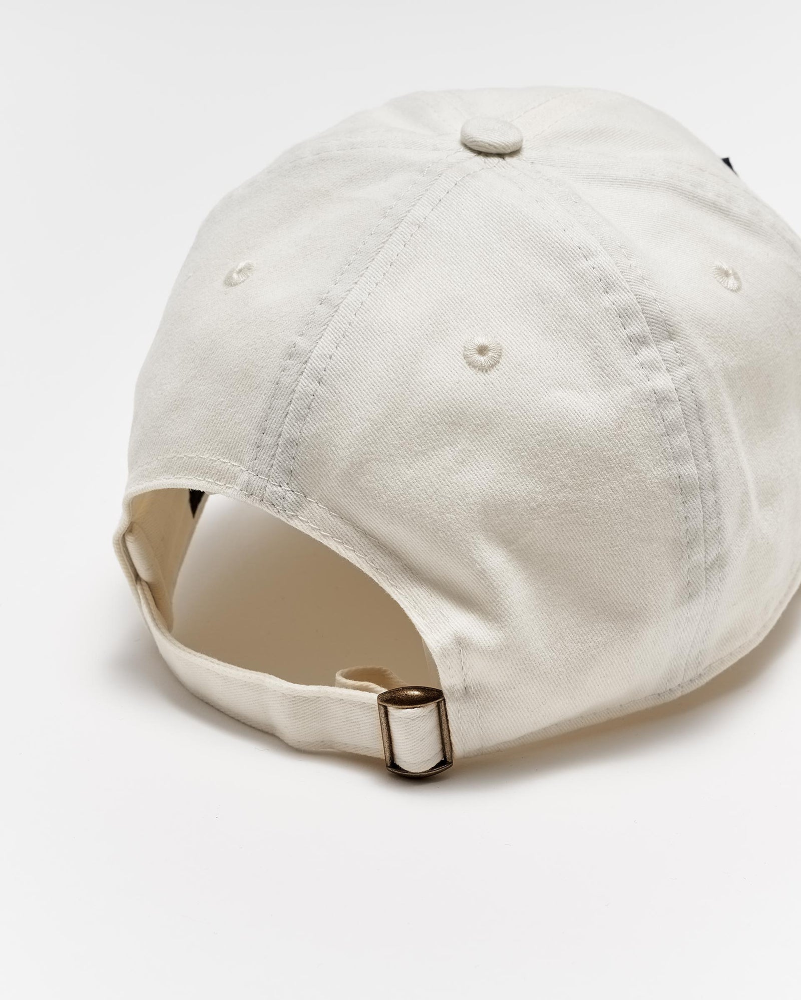 A beige baseball cap viewed from the back, showing an adjustable strap with a metal buckle and stitched ventilation holes on the crown, set against a white background.