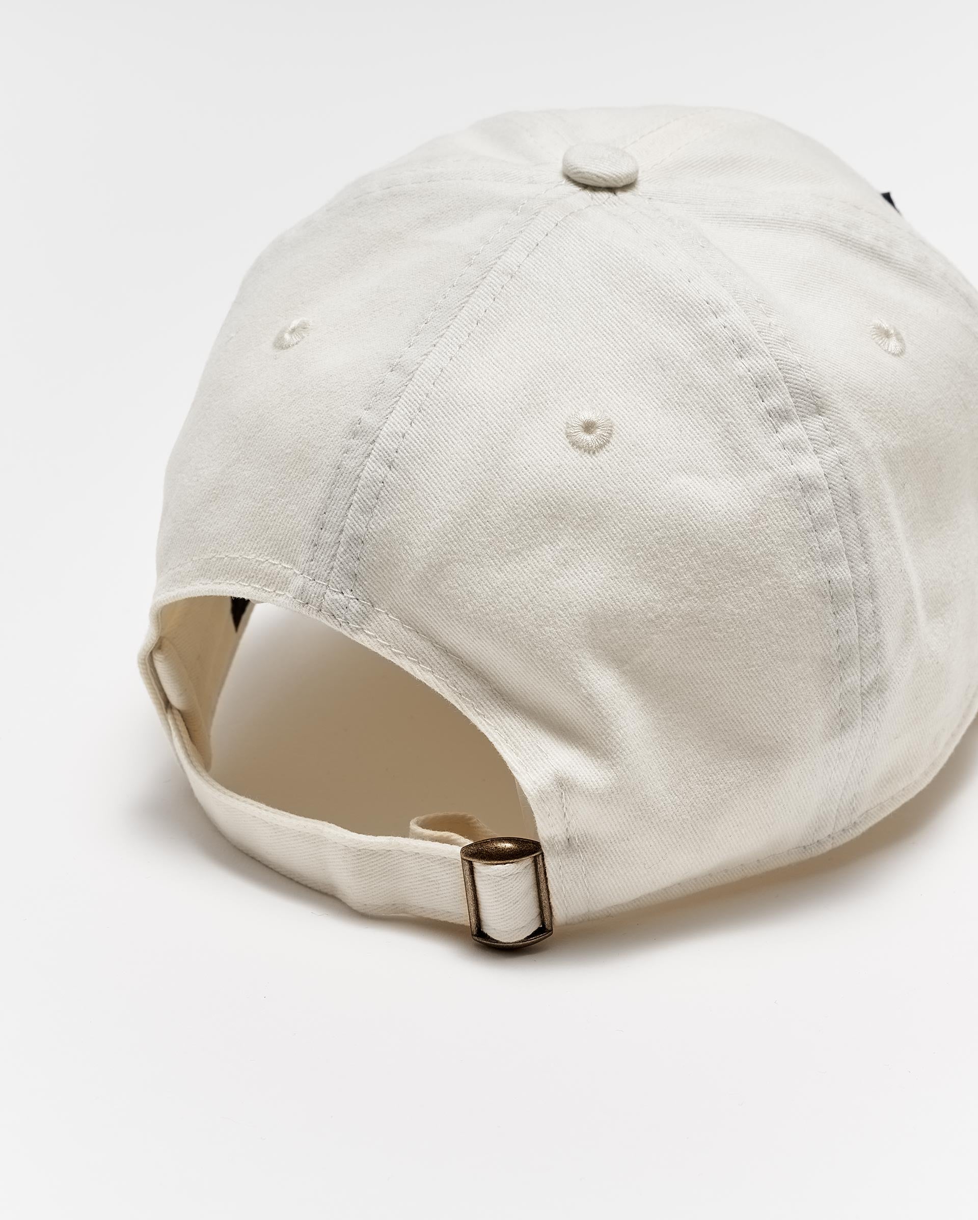 A beige baseball cap viewed from the back, showing an adjustable strap with a metal buckle and stitched ventilation holes on the crown, set against a white background.