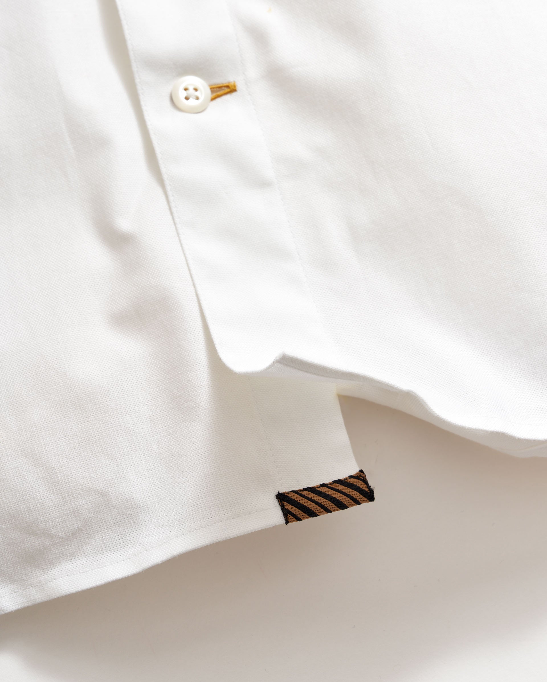 Close-up of a white shirt with a button and collar detail on a light background