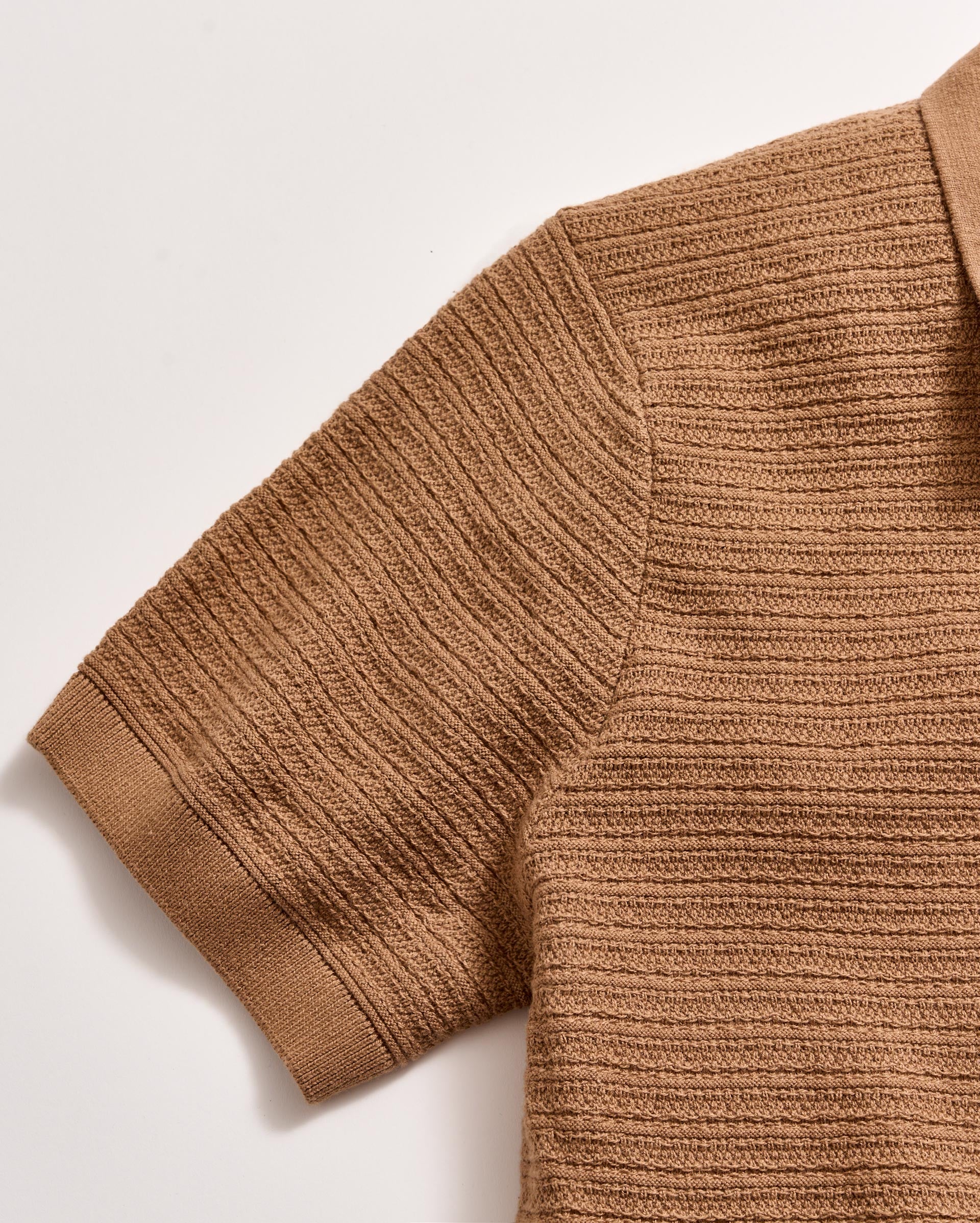 Close-up of a brown knitted sweater sleeve on a light background