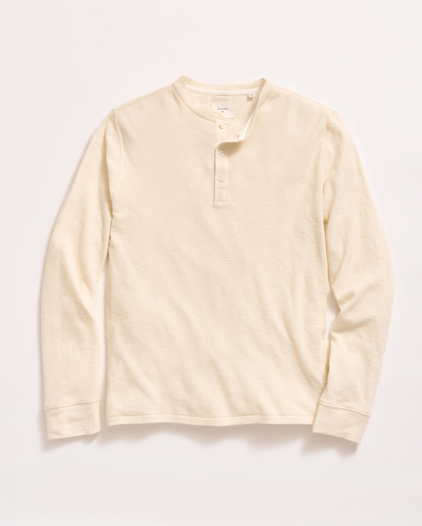 A long-sleeve, cream-colored henley shirt with a round neckline and three buttons down the front, laid flat on a white background.