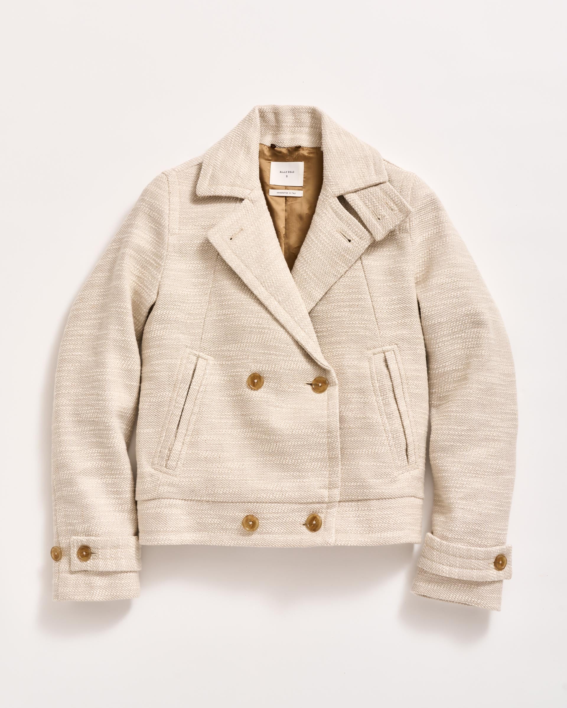 A cream-colored, double-breasted wool jacket with brown buttons, two front pockets, a notched collar, and buttoned cuffs, laid flat on a white background.