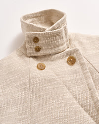 A close-up of a cream-colored textured coat with a high, structured collar and large tan buttons arranged in a double-breasted style against a plain white background.