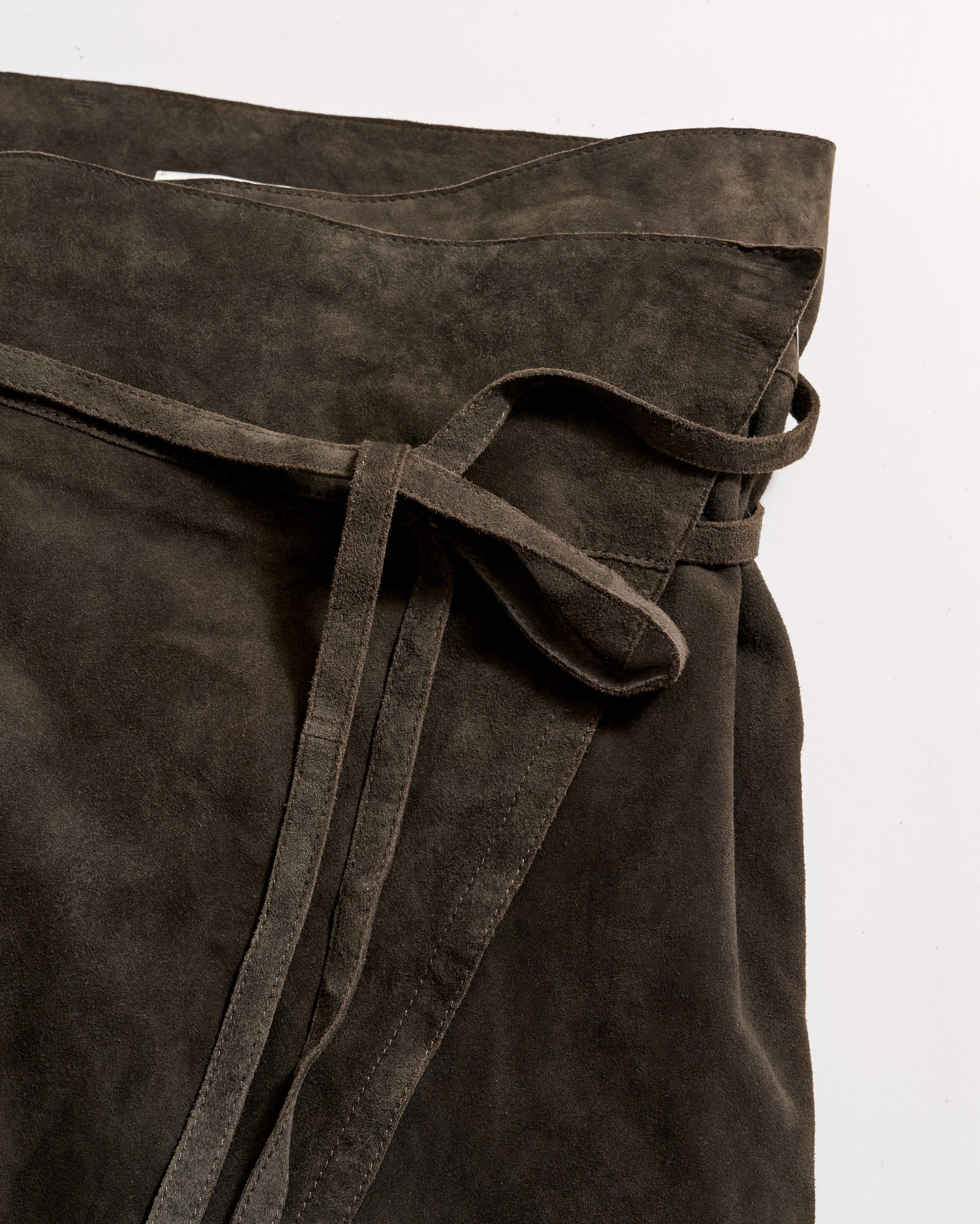 A close-up of a dark brown suede wrap skirt with a tied belt detail, laid flat on a white surface.