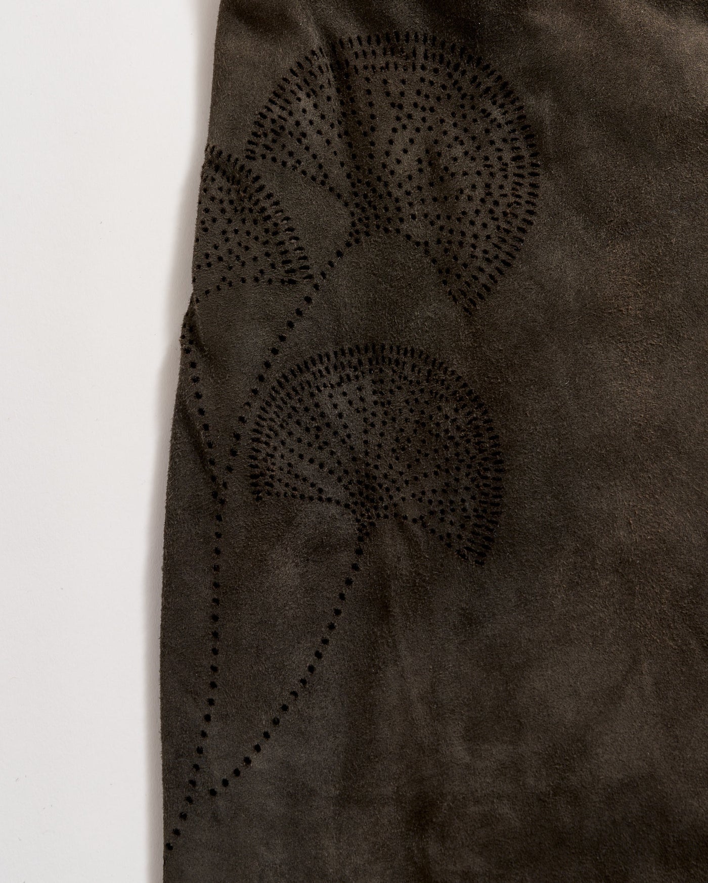 A close-up of dark brown suede fabric featuring a subtle, decorative pattern of three fan-shaped leaves created with small, evenly spaced black dots.