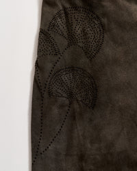 A close-up of dark brown suede fabric featuring a subtle, decorative pattern of three fan-shaped leaves created with small, evenly spaced black dots.