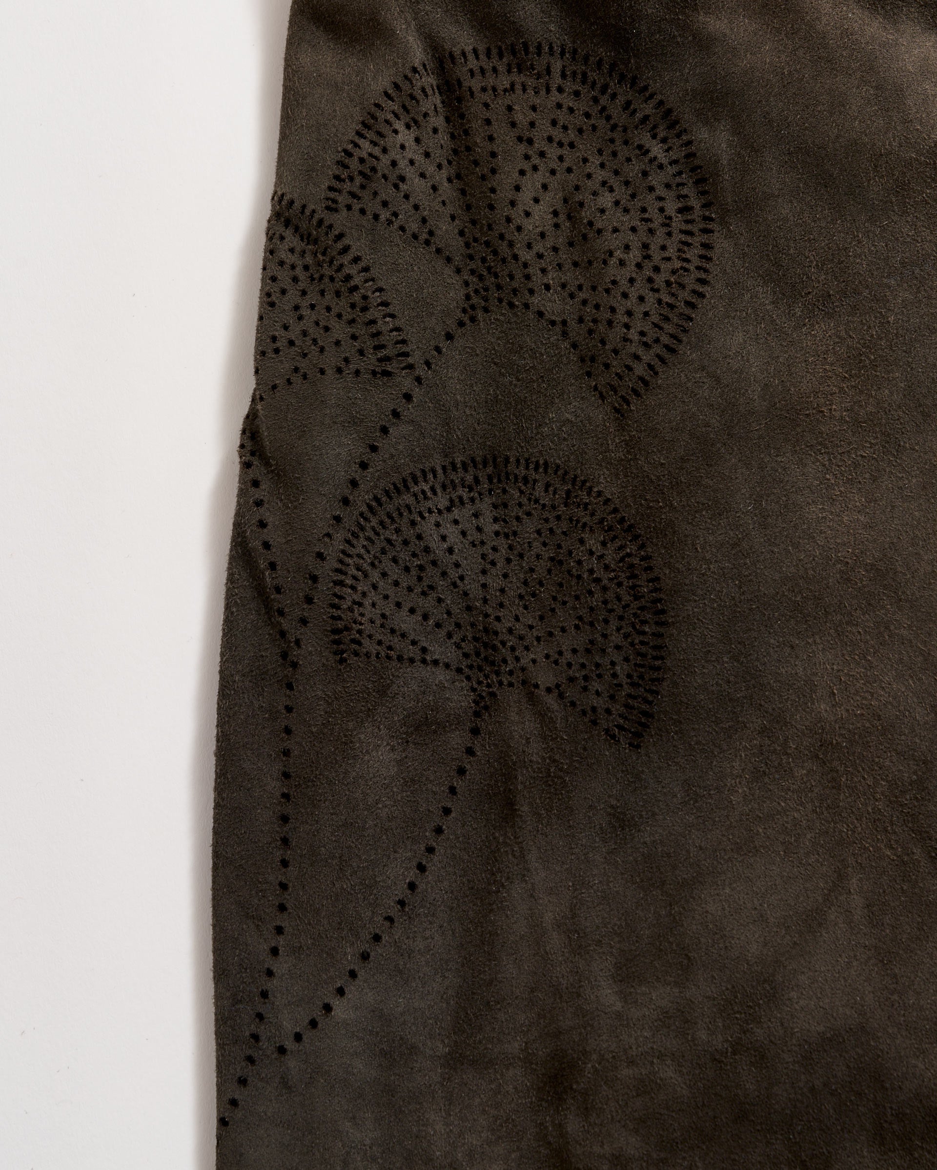 A close-up of dark brown suede fabric featuring a subtle, decorative pattern of three fan-shaped leaves created with small, evenly spaced black dots.