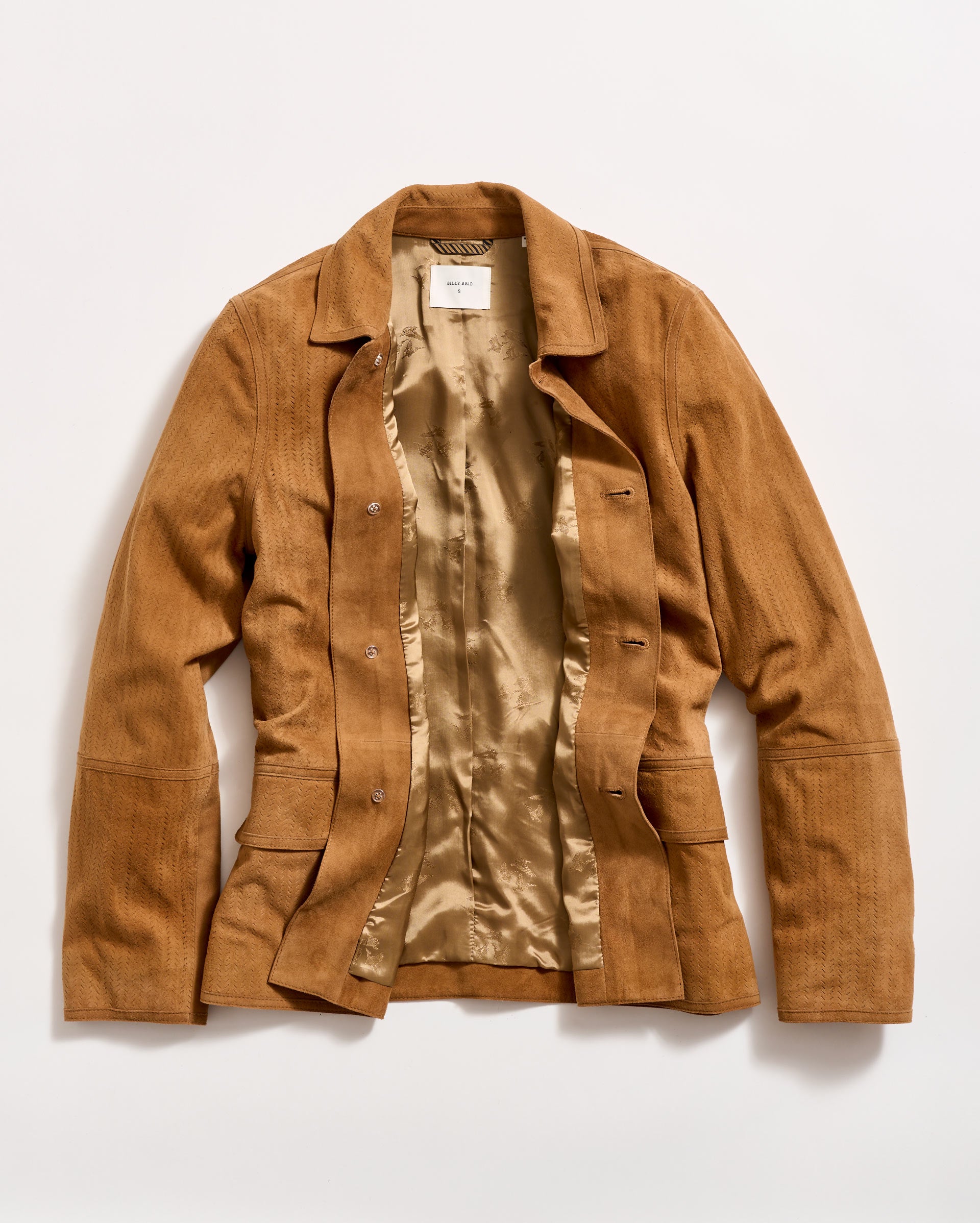 A light brown suede jacket with a shiny beige satin lining is laid flat on a white background. The jacket is unbuttoned, showing the inside and the front pockets.