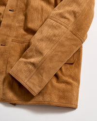 Close-up of a tan suede jacket sleeve with visible stitching and textured pattern. The jacket has a pocket and detailed seam lines, displayed on a white background.