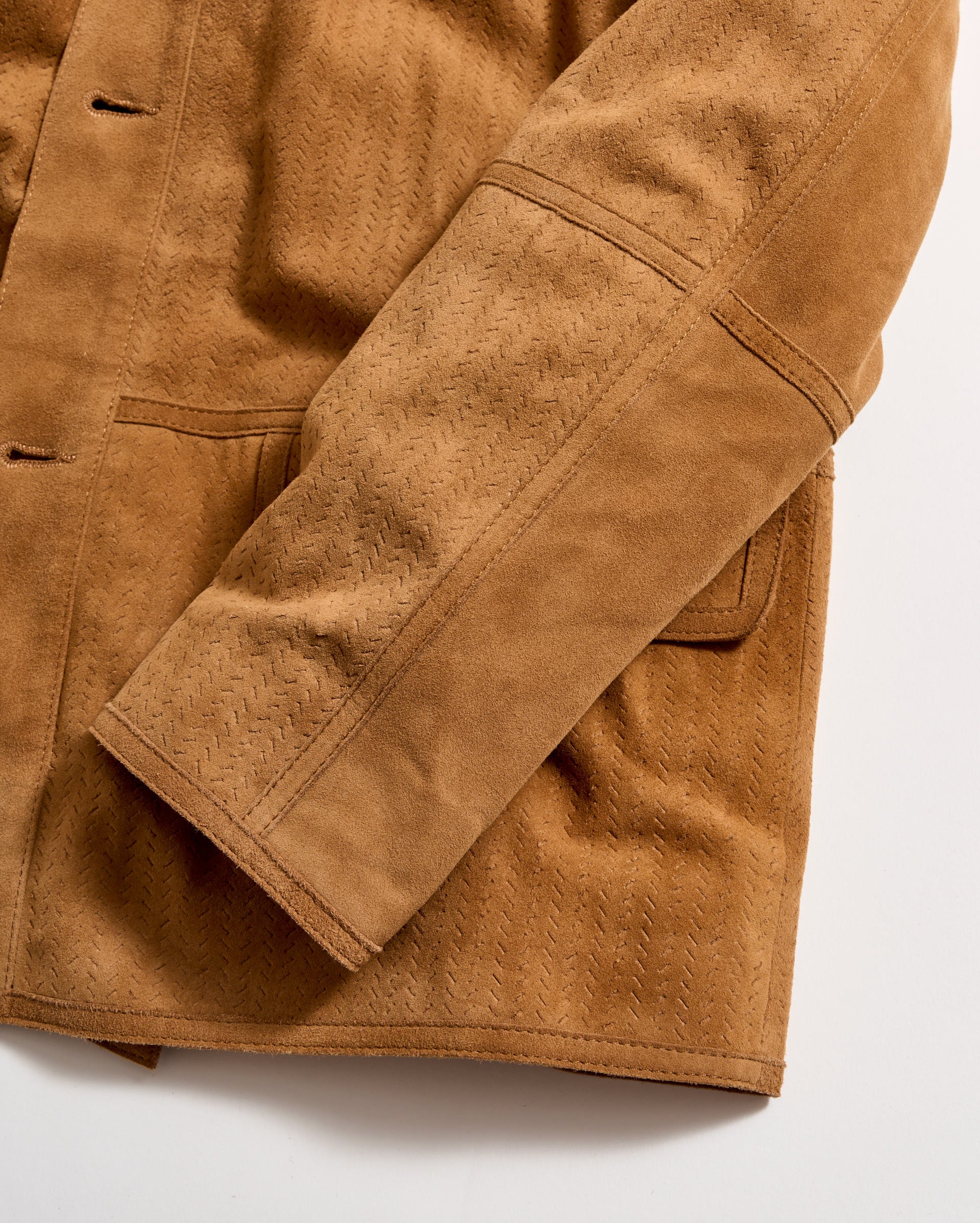 Close-up of a tan suede jacket sleeve with visible stitching and textured pattern. The jacket has a pocket and detailed seam lines, displayed on a white background.