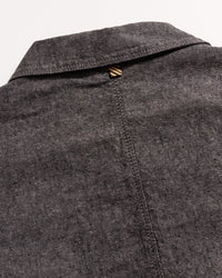 Close-up of the back of a grey textured collared shirt, showing a seam running down the center and a small brown and beige striped loop at the top below the collar.