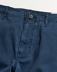 Close-up of the waistband and fly area of a pair of blue pants with a button closure and belt loops, shown on a light background.