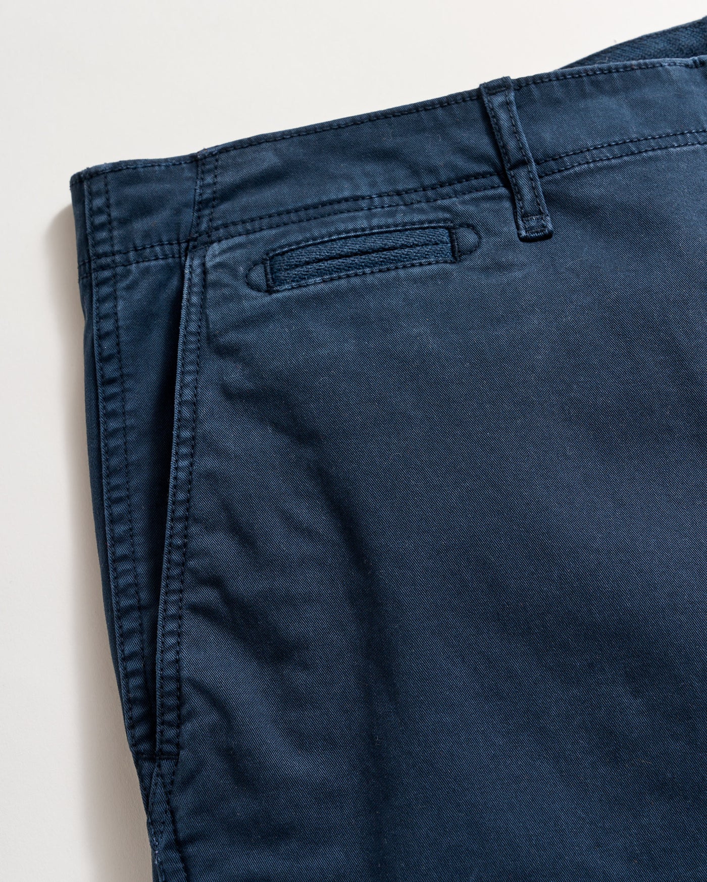 Close-up view of a pair of dark blue pants, showing the waistband, belt loop, and a welt pocket on a light background.