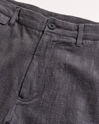 Close-up of the waistband and upper section of a pair of gray textured pants with a button closure and belt loops, set against a light background.