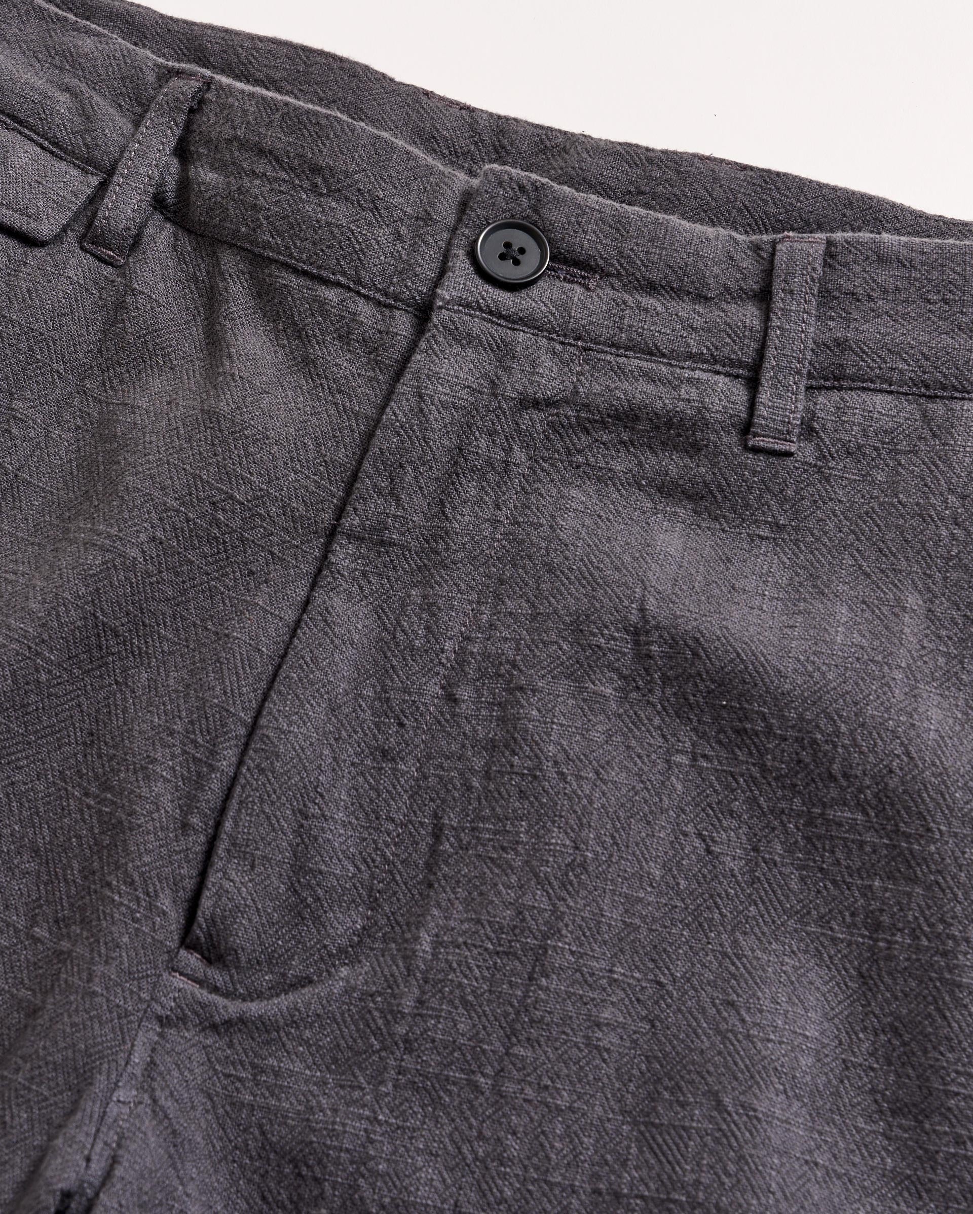 Close-up of the waistband and upper section of a pair of gray textured pants with a button closure and belt loops, set against a light background.