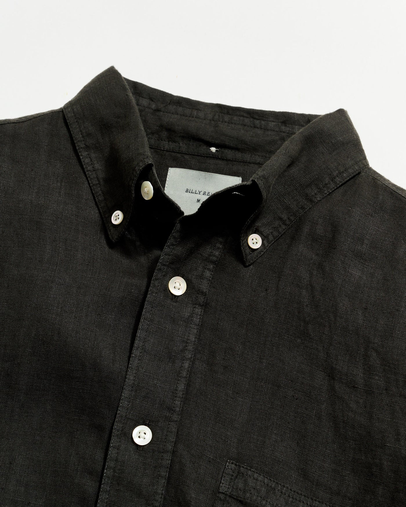Close-up of a black button-up shirt with a visible brand label on a light gray background