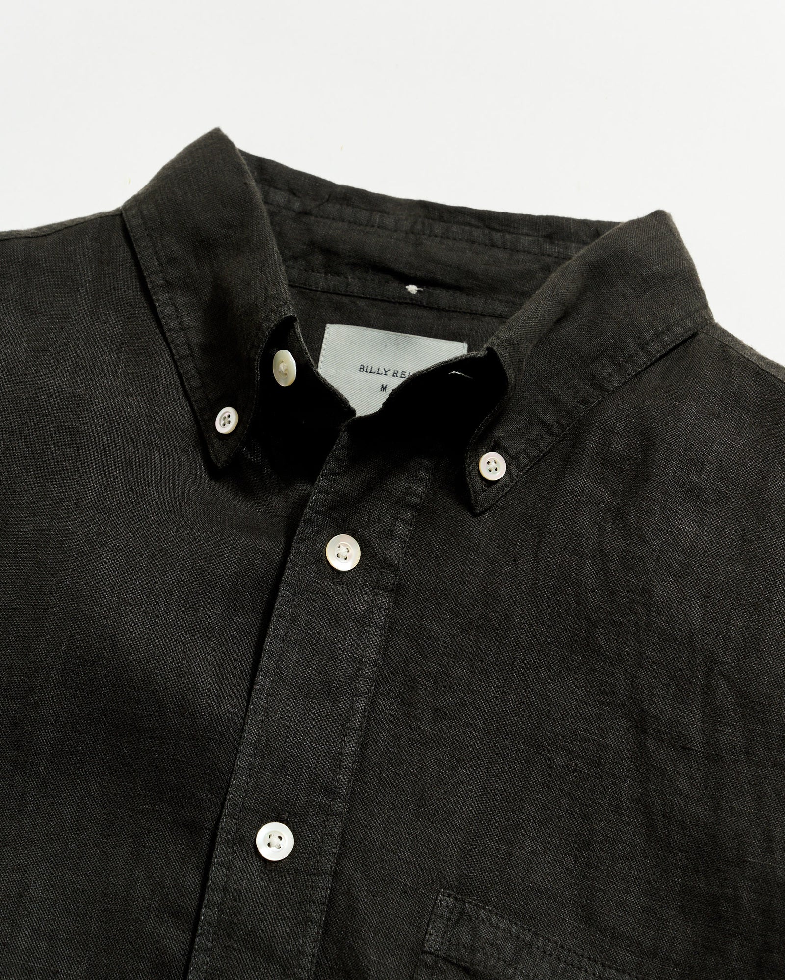 Close-up of a black button-up shirt with a visible brand label on a light gray background