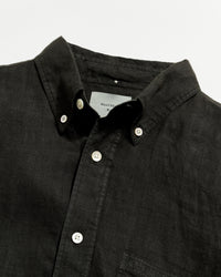 Close-up of a black button-up shirt with a visible brand label on a light gray background