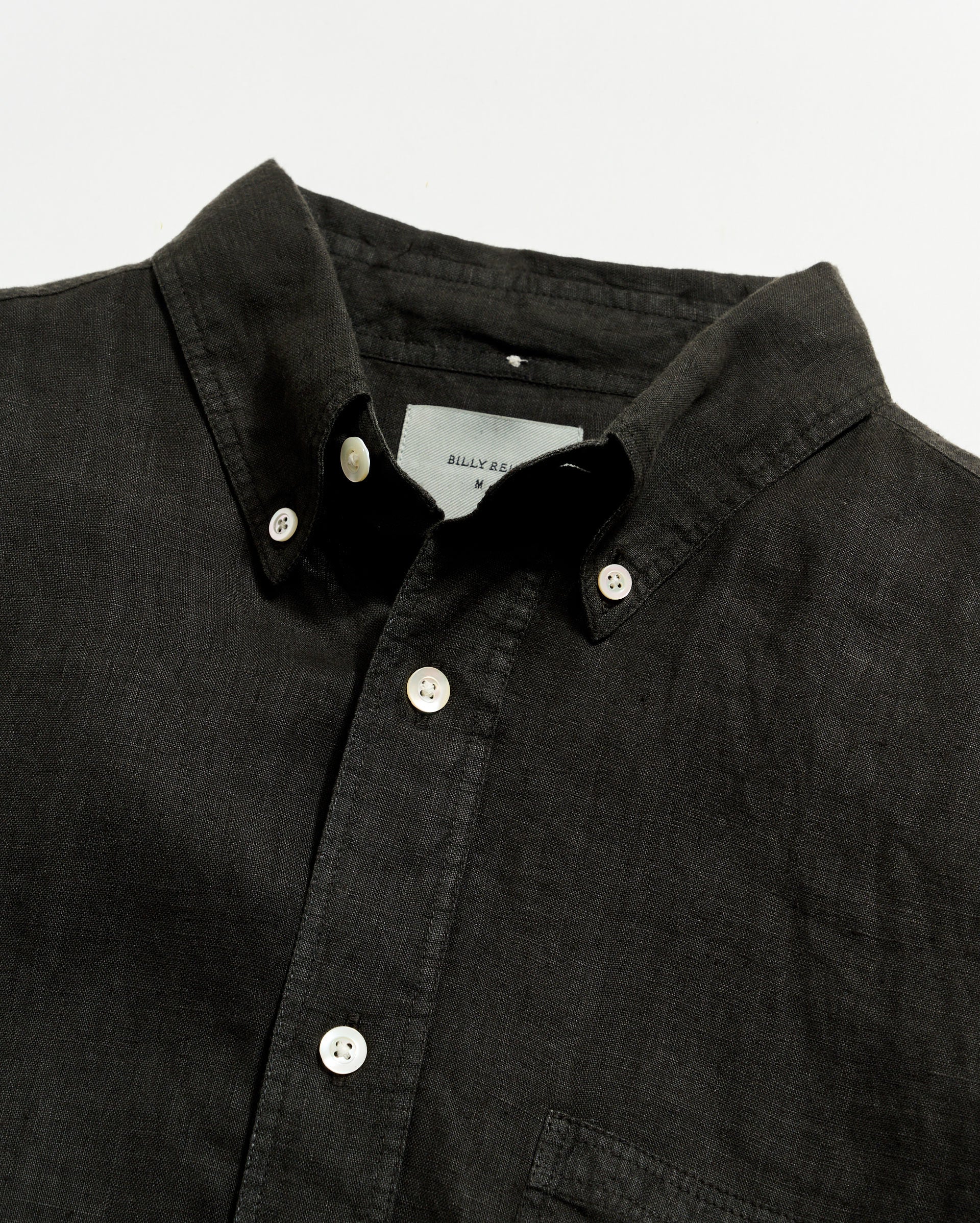 Close-up of a black button-up shirt with a visible brand label on a light gray background