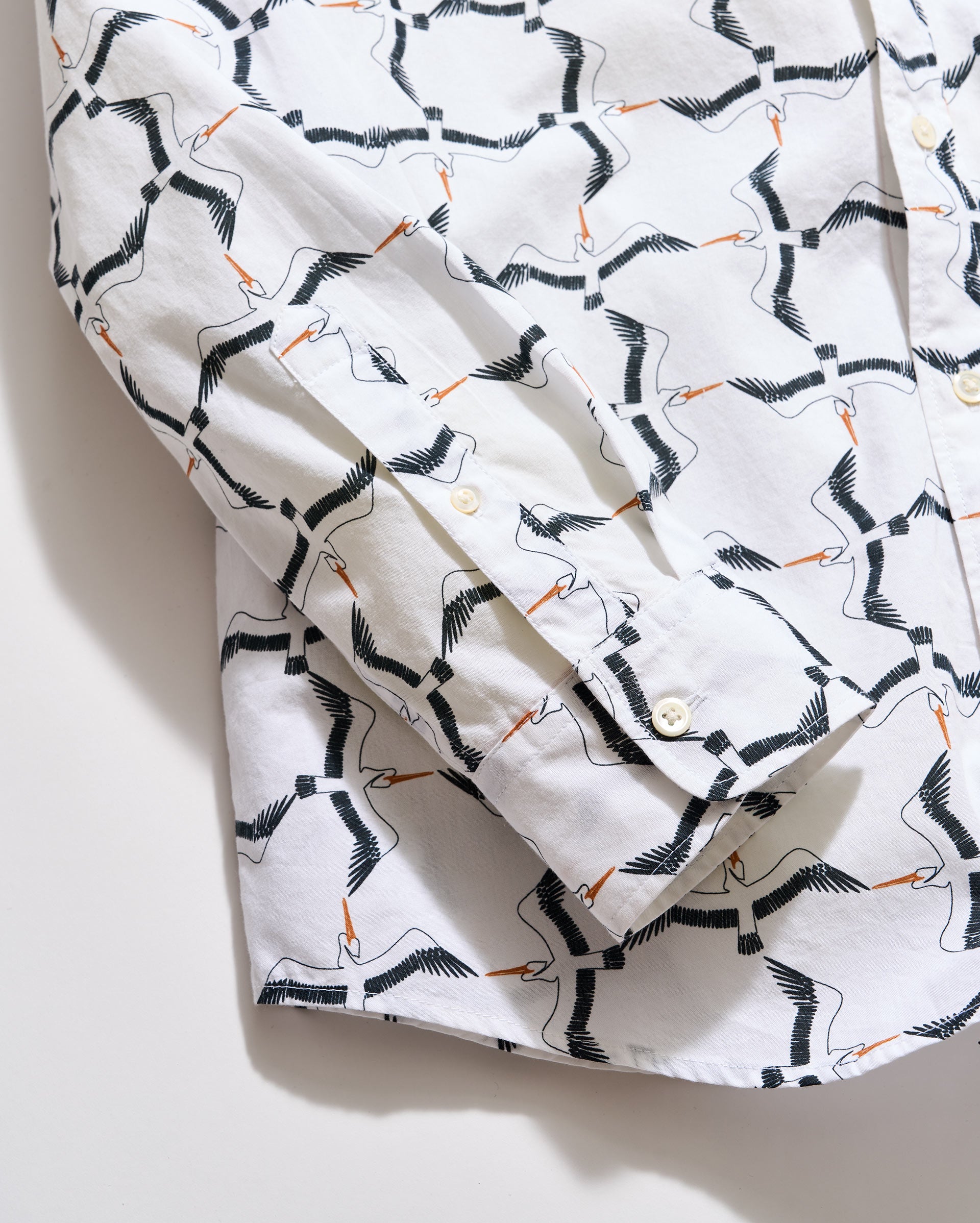 White shirt with black and orange bird pattern on a light gray background